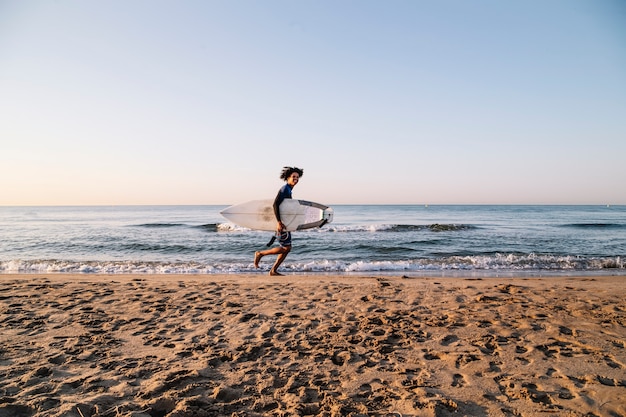 Afro surfista che corre con tavole da surf lungo la riva