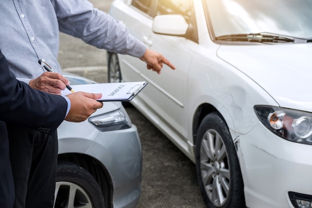 Agente assicurativo esamina l&#39;auto danneggiata e presenta il modulo di richiesta di rimborso dopo l&#39;incidente