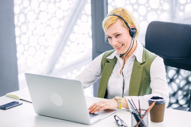 Agente di call center femminile sorridente e amichevole con auricolare che lavora sulla hotline di supporto in ufficio