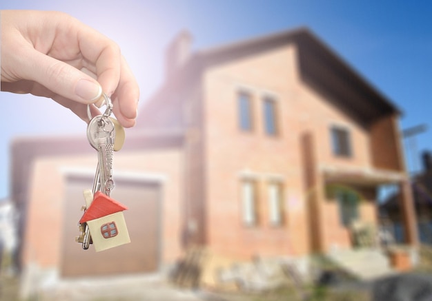 Agente immobiliare che consegna una chiave di casa Chiave con un portachiavi a forma di casa su sfondo di una nuova casa Concetto di ipoteca