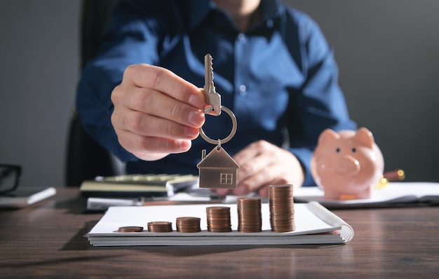 Agente immobiliare che mostra la chiave di casa sopra la pila di monete.