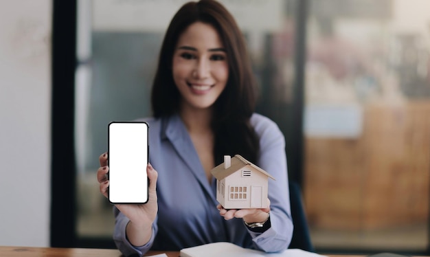 Agente immobiliare che mostra un modello di casa e un telefono cellulare con schermo bianco vuoto per la pubblicità
