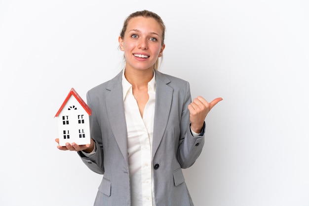 Agente immobiliare donna in possesso di una casa giocattolo isolata su sfondo bianco che punta al lato per presentare un prodotto
