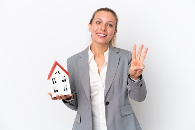 Agente immobiliare donna in possesso di una casa giocattolo isolata su sfondo bianco felice e contando tre con le dita