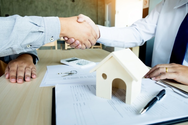 Agente immobiliare in tuta seduta in una scrivania in ufficio stringendo la mano con il cliente dopo la firma del contratto