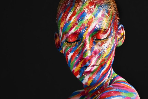 Aggiungi un tocco di colore alla tua routine di bellezza Foto in studio di una giovane donna in posa con una vernice dai colori vivaci sul viso su uno sfondo nero