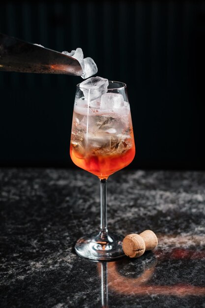 Aggiunta di ghiaccio in aperol spritz per preparare un cocktail in un bar