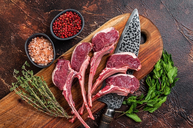 Agnello crudo, costolette di montone bistecche su una tavola di legno. Sfondo scuro. Vista dall'alto.