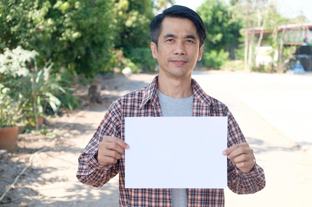 Agricoltore asiatico sorridente che tiene un segno bianco alla fattoria