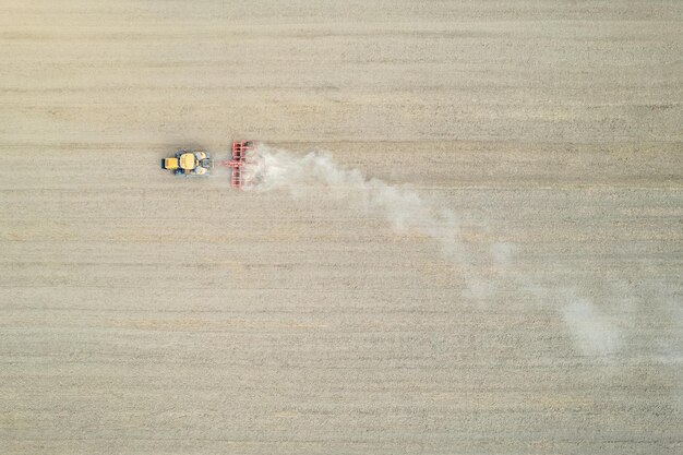 Agricoltore che guida un moderno trattore cingolato giallo che erpica e livella il terreno asciutto per la prossima semina nei campi di pianura rurali