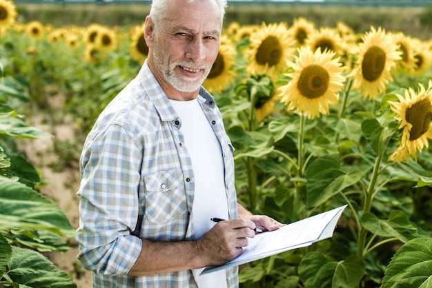 Agricoltore che ispeziona il giorno soleggiato di estate del giacimento del girasole