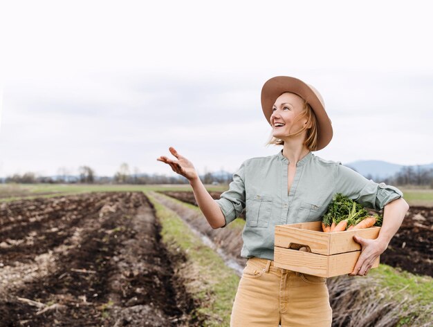 Agricoltore donna con una scatola di legno piena di verdure fresche crude in un campo agricolo