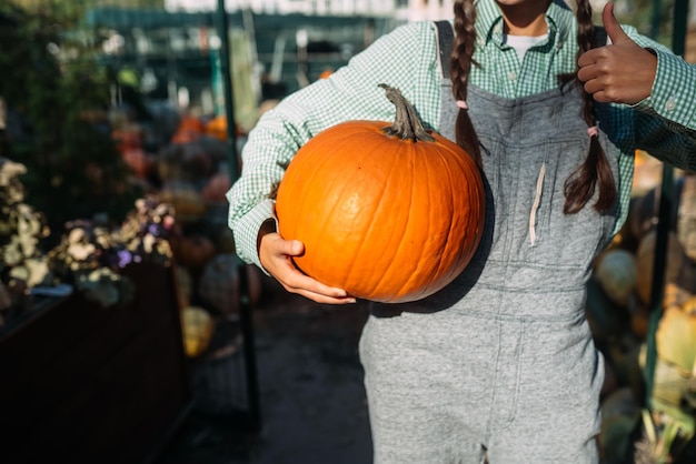 Agricoltore femminile che tiene la zucca matura e che mostra il pollice in su