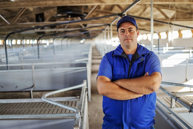 Agricoltore in piedi nel fienile vuoto con le braccia incrociate. Agricoltore che prepara il fienile per il concetto di animali.