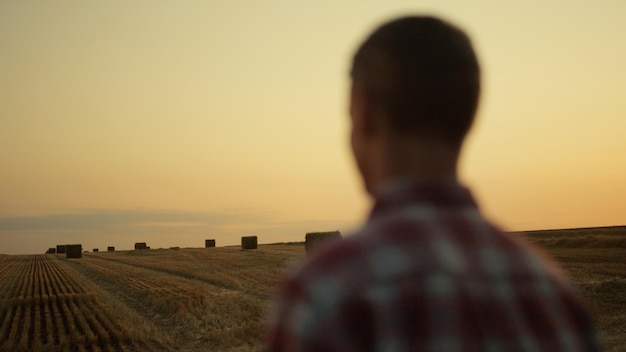 Agricoltore in piedi pagliaio campo tramonto dorato vista posteriore Concetto di agricoltura