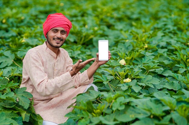 Agricoltore indiano che mostra lo schermo dello smartphone al campo agricolo.