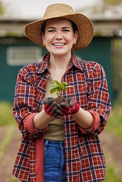 Agricoltore sostenibile che tiene una pianta o una piantina all'aperto sorridente e felice della sua fattoria o giardino biologico Giovane attivista della natura femminile appassionata di sostenibilità in piedi su un terreno agricolo