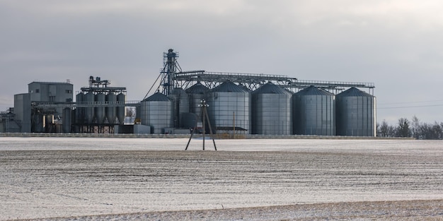 Agro silos ascensore per granaio in giornata invernale in campo nevoso Silos su impianto di produzione agroprocessing per la lavorazione, essiccazione, pulizia e stoccaggio di prodotti agricoli farina cereali e grano