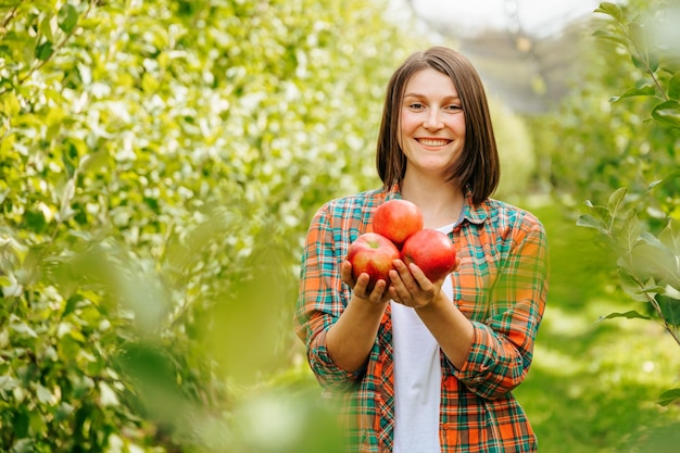 Agronomo carino donna con le mele nelle sue mani sorridenti sta nel giardino dopo il raccolto