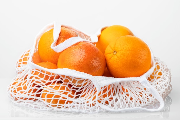 Agrumi nella borsa di corda bianca isolata su fondo bianco. Arancia, pompelmo, mandarino. Niente plastica.