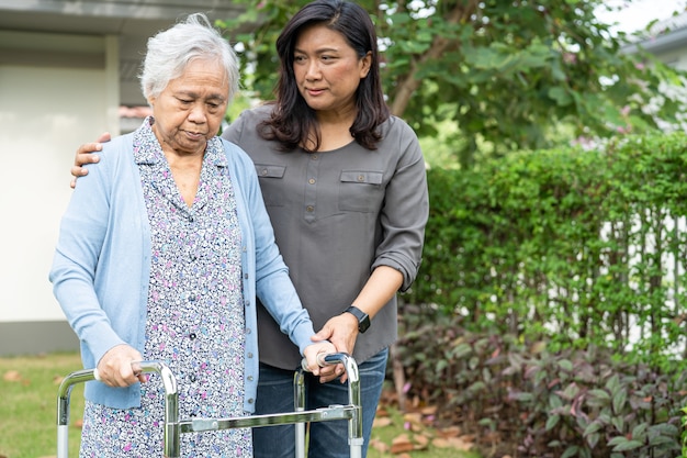 Aiutare e prendersi cura della donna asiatica senior utilizzare walker mentre si cammina in giardino in casa