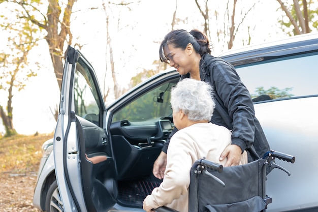 Aiutare e sostenere la donna senior asiatica seduta in sedia a rotelle in macchina.