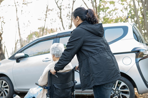 aiutare e supportare una paziente asiatica anziana seduta su una sedia a rotelle prepararsi a raggiungere la sua auto