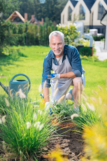 Aiutare in giardino. Bel marito sorridente ampiamente mentre si sente estremamente felice di aiutare la moglie in giardino