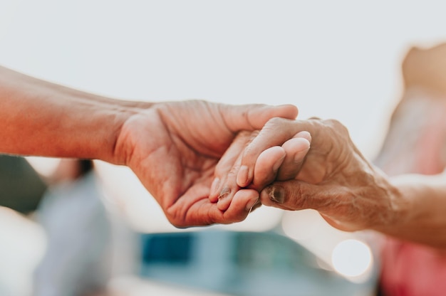 Aiutare le mani anziane, prendersi cura del concetto di anziani. Vecchi e giovani che si tengono per mano su sfondo chiaro.