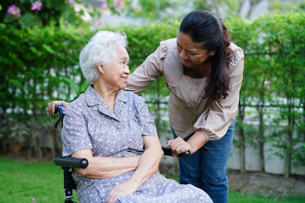 Aiuto del caregiver Paziente con disabilità della donna anziana asiatica seduto su sedia a rotelle nel concetto medico del parco