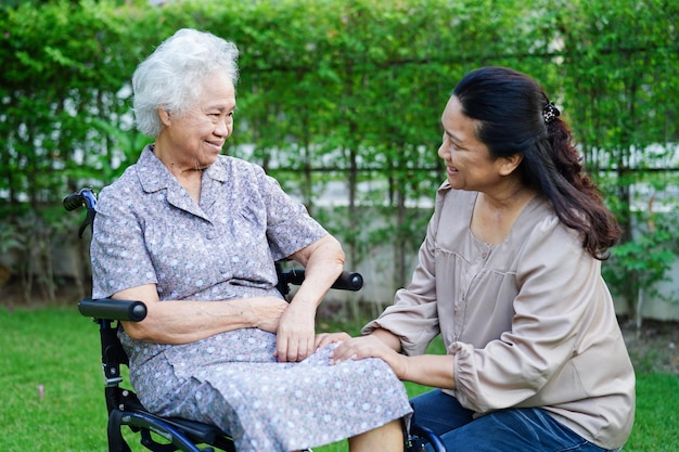 Aiuto del caregiver Paziente con disabilità della donna anziana asiatica seduto su sedia a rotelle nel concetto medico del parco