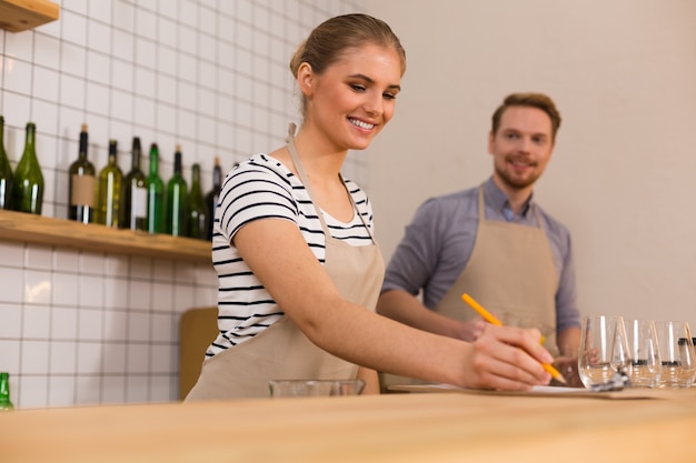 Al lavoro. Gioiosa e positiva giovane donna sorridente e guardando i suoi appunti mentre si lavora nella caffetteria