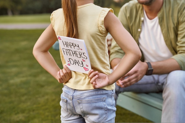 Al miglior papà del mondo bambina che nasconde una cartolina fatta a mano per suo padre mentre spende