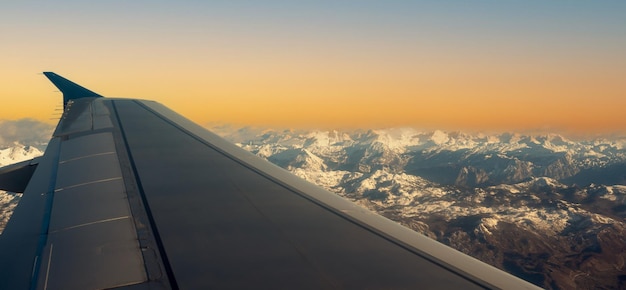 Ala dell'aereo sopra la copertura della montagna con neve bianca. tramonto colorato da una vista in aereo. Vista dall'aeroplano sulle montagne innevate della superficie terrestre. Vista aerea delle Alpi dall'aeroplano.