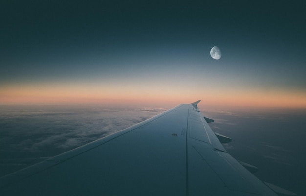 Ala di un aeroplano che vola al mattino presto con la luna ancora nel cielo