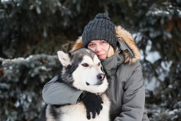 Alaskan malamute che abbraccia con la donna nella foresta di inverno