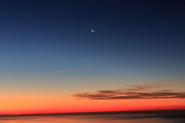 Alba all'orizzonte con nuvole di mare e la luna calante