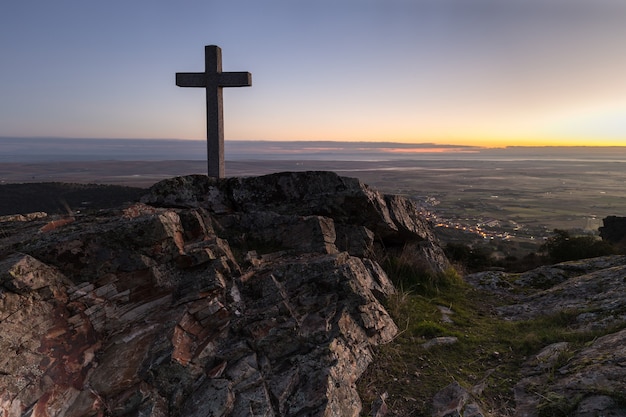 Alba con croce in primo piano accanto alla Sierra de Fuentes. Spagna.