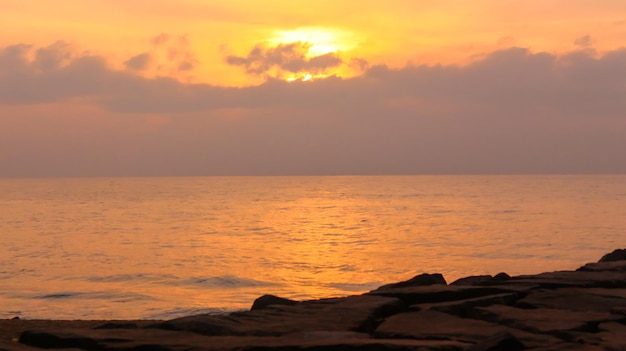 Alba di colore giallo dorato nella spiaggia di Pondicherry con rocce