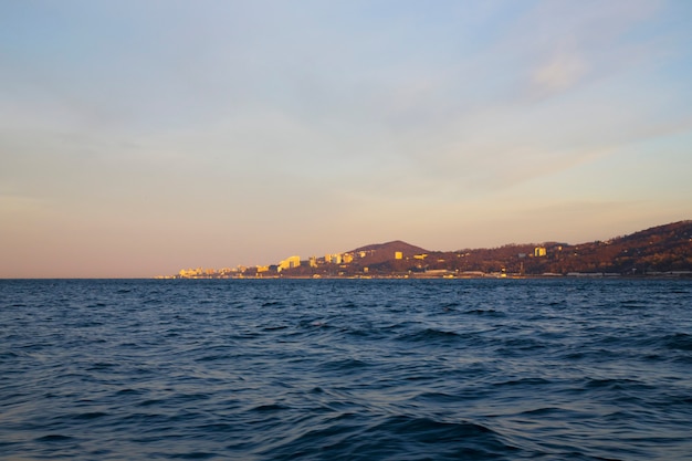 Alba nella foschia rosa del mare del sole che sorge sulla città del mare e sulle montagne all'orizzonte