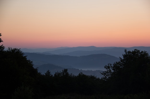 Alba nelle montagne dei Carpazi. Montagne scure nella nebbia mattutina sullo sfondo del cielo luminoso.