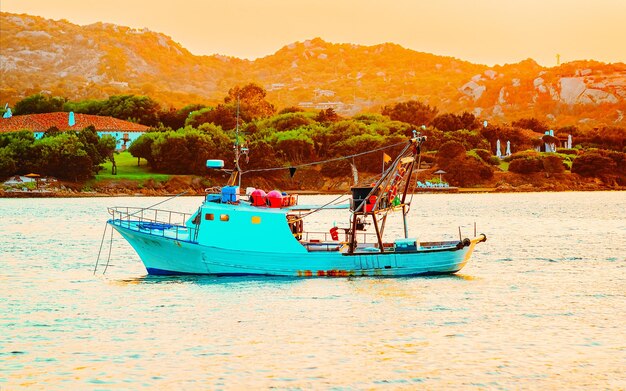 Alba o tramonto con yacht a Porto Rotondo in Costa Smeralda al Mar Mediterraneo in Sardegna, isola d'Italia. Barca in Sardegna in estate. Paesaggio della provincia di Olbia. Tecnica mista.
