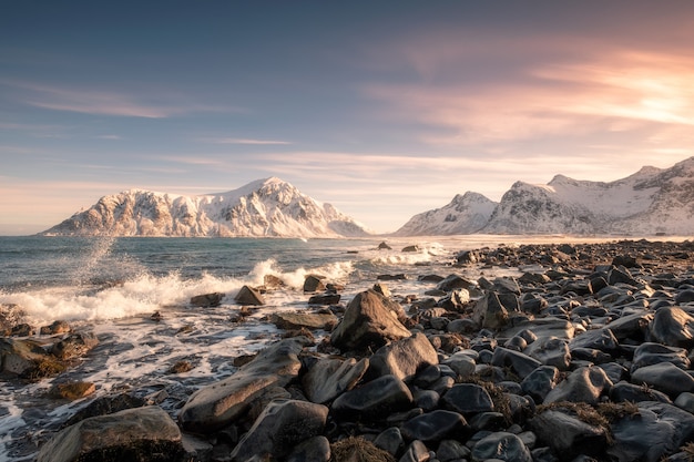 Alba variopinta della catena montuosa della neve con l&#39;onda che colpisce sulla linea costiera alla spiaggia di Skagsanden