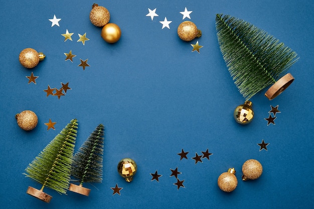 Alberi di Natale, palle di natale dorate, fiocchi di neve e stelle su sfondo blu. Lay piatto, vista dall'alto, copia spazio. Cornice di Natale, mockup di banner di Capodanno