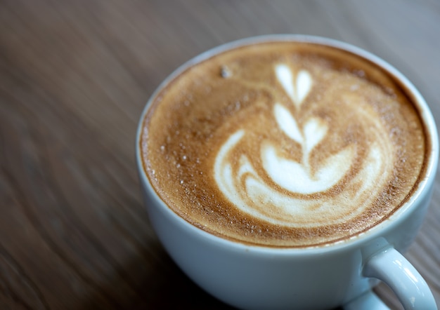 Albero del cuore del caffè di Latte in tazza bianca disposta su un pavimento di legno.