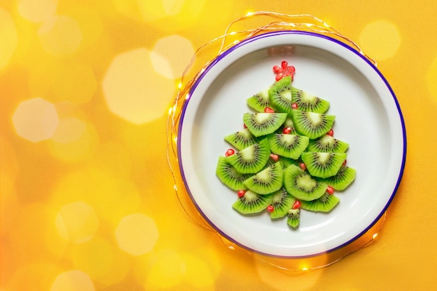 Albero di Natale commestibile fatto di kiwi e melograno su tovaglia gialla con luce ghirlanda