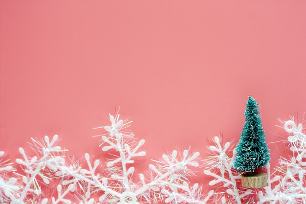 Albero di natale con gli ornamenti del fiocco di neve su fondo rosa per il giorno di Natale e conce di feste