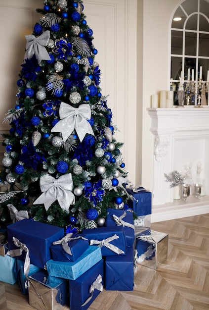 Albero di Natale decorato con giocattoli blu e fiocchi a casa vicino al camino