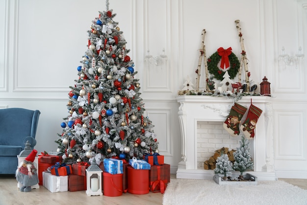 Albero di Natale decorato e scatole regalo rosse accanto al camino bianco decorato