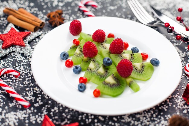 Albero di Natale del kiwi con lampone, mirtillo e mirtillo rosso sul tavolo con decorazione